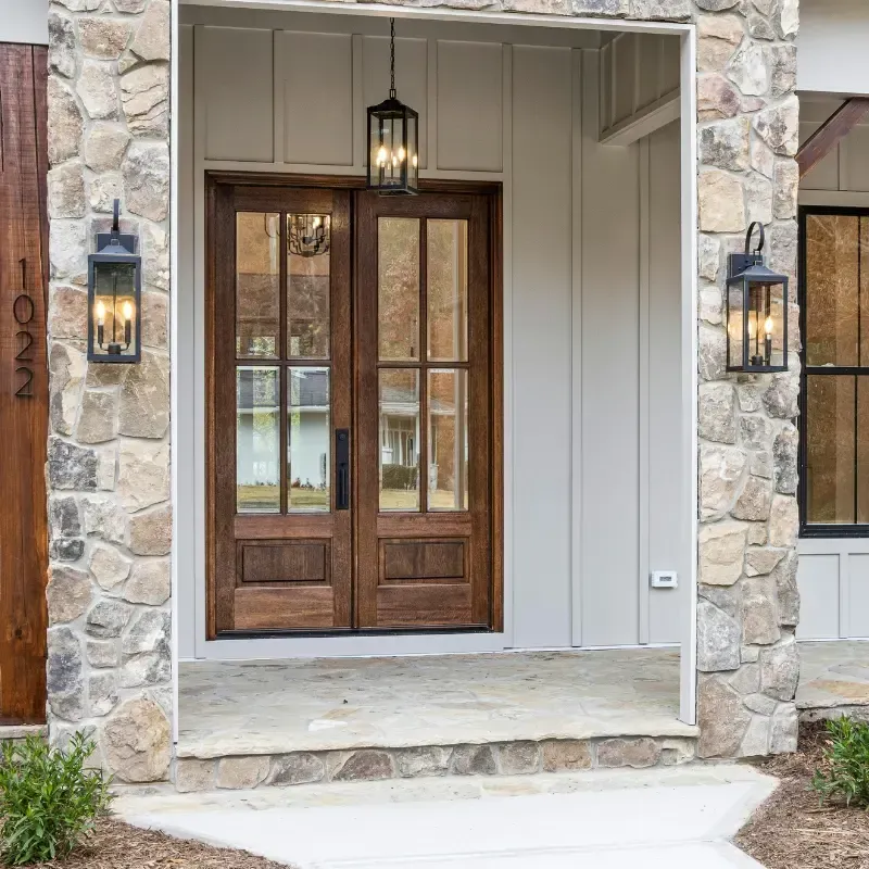 Entrada de casa de campo de piedra y madera con puertas dobles de cristal, apliques y lámpara colgante.