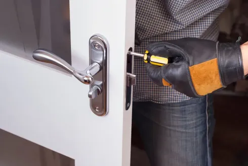 Persona usando un destornillador para ajustar la cerradura de una puerta blanca.