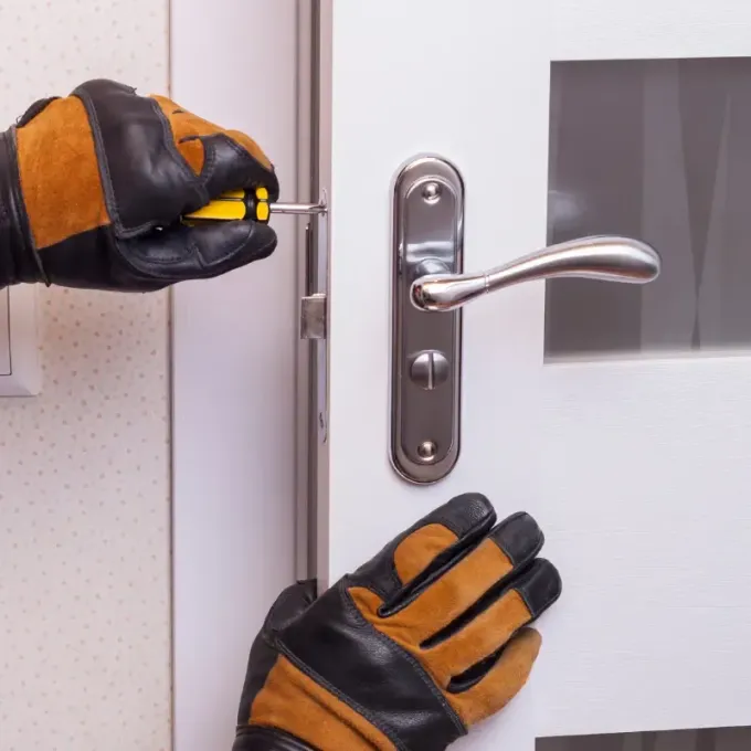 Manos con guantes de trabajo instalando una manija de puerta con un destornillador. Puerta blanca.