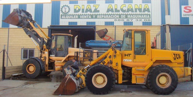 Dos tractores amarillos están estacionados frente a un edificio que dice Díaz Alcana.