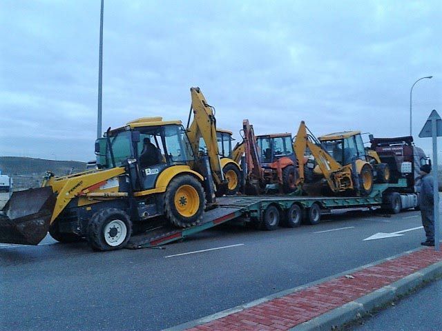 Un grupo de tractores amarillos están en un remolque al costado de la carretera.