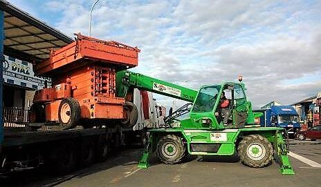 Una grúa verde está cargando un camión volquete rojo en un tren.