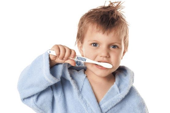 Niño con un albornoz azul sosteniendo un cepillo de dientes en la boca sobre un fondo blanco