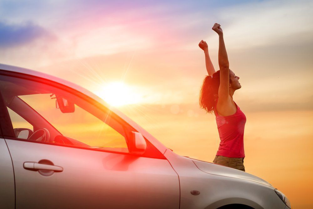 Una persona estirando junto a un coche plateado al atardecer, con un cielo naranja cálido de fondo