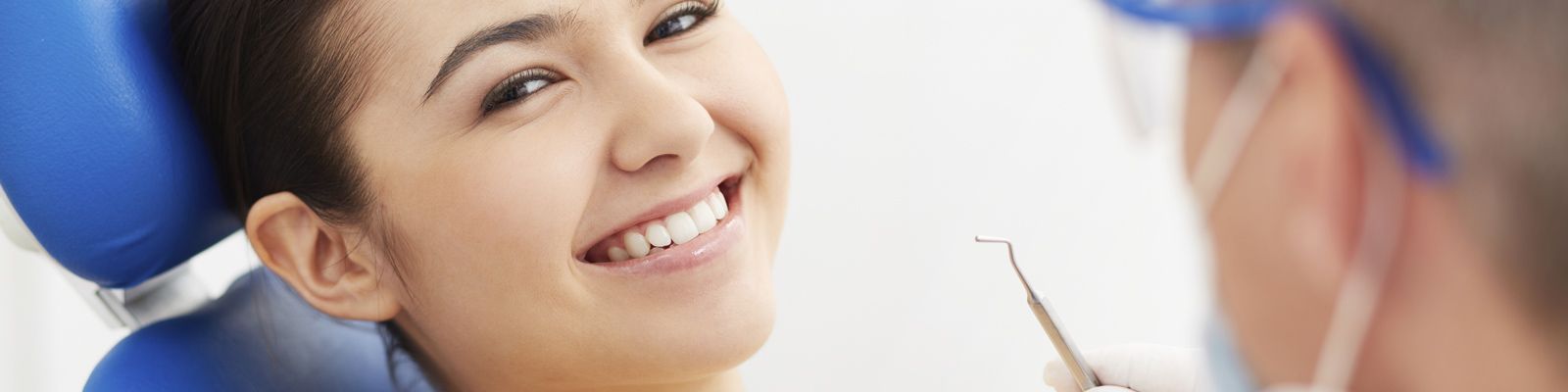 Paciente sonriente recostada en el sillón mientras el dentista le examina los dientes
