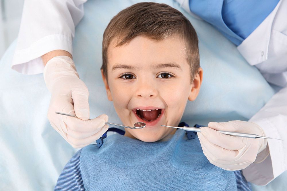 Dentista examinando los dientes de un niño sonriente con un espejo dental y las manos enguantadas