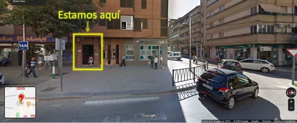 Vista de la calle con una puerta resaltada en amarillo y un cartel de «Estamos aquí» que señala una ubicación.