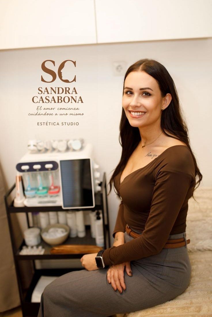 Una mujer sentada junto a una máquina de café en la recepción de un spa sonríe a la cámara.