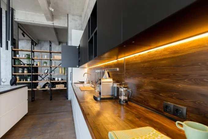 Cocina moderna con encimeras de madera, gabinetes negros y estantes abiertos en un espacio estilo loft.