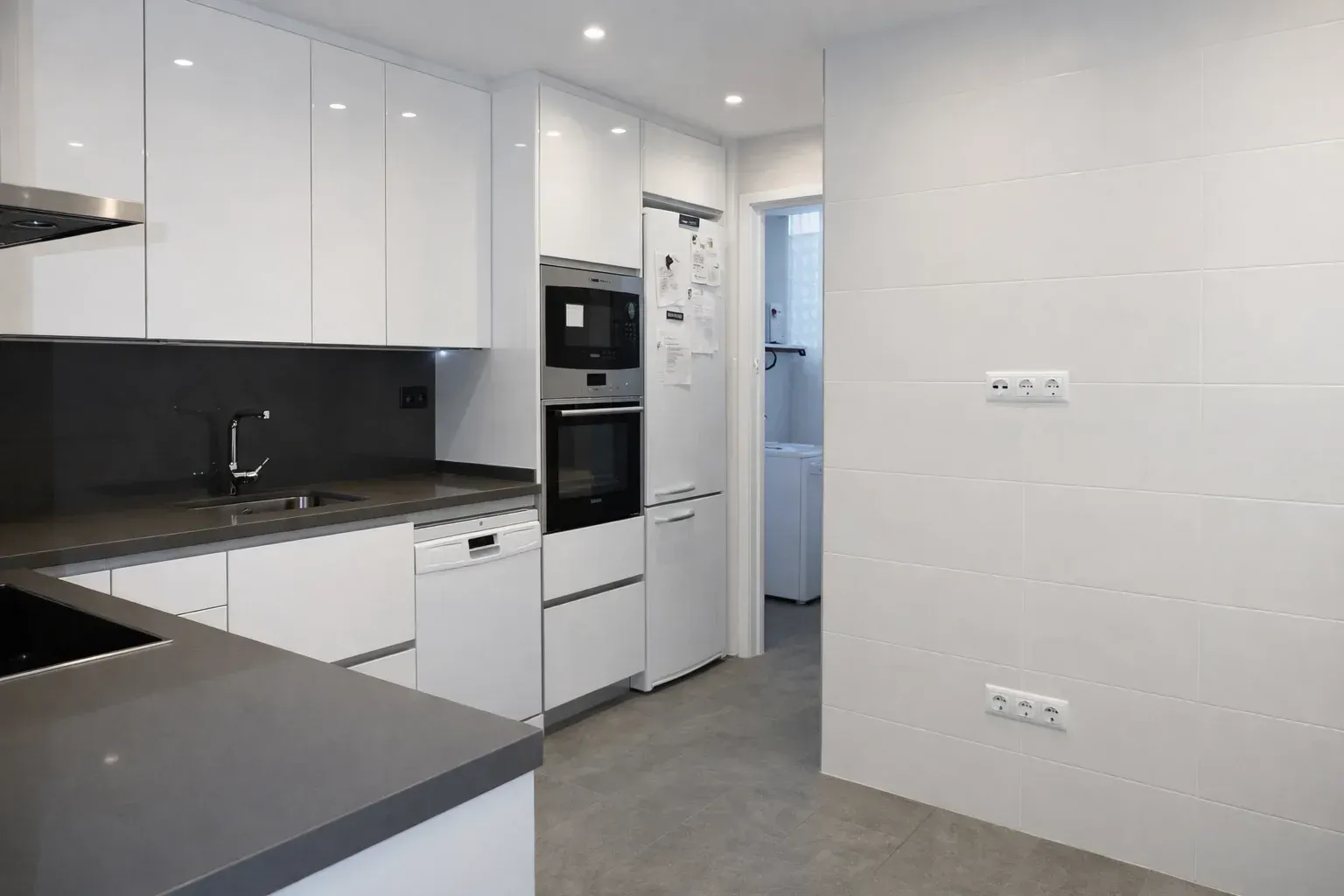 Cocina blanca moderna con encimeras, electrodomésticos y piso grises.