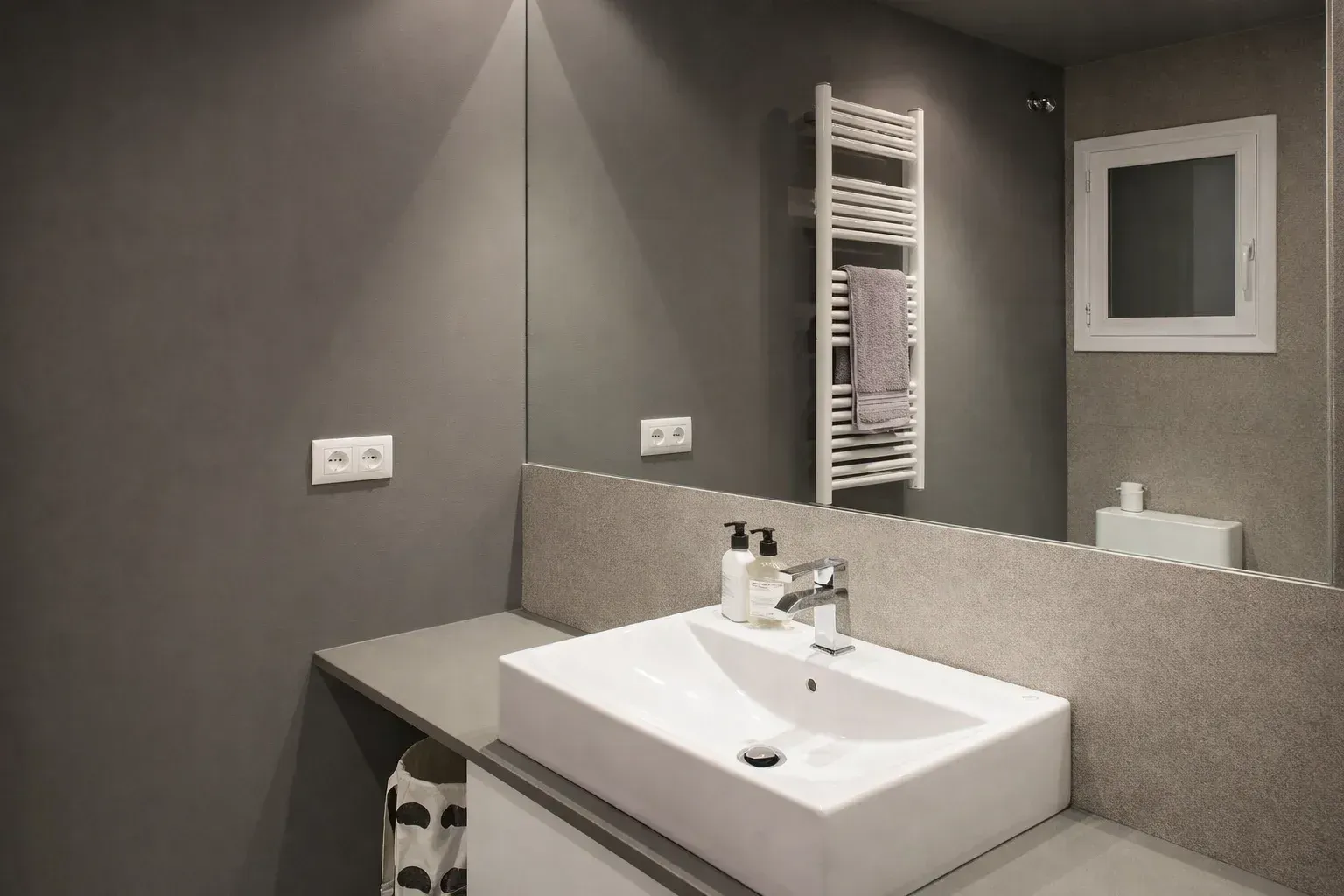 Baño moderno con paredes grises, lavabo rectangular blanco, espejo grande y toallero.