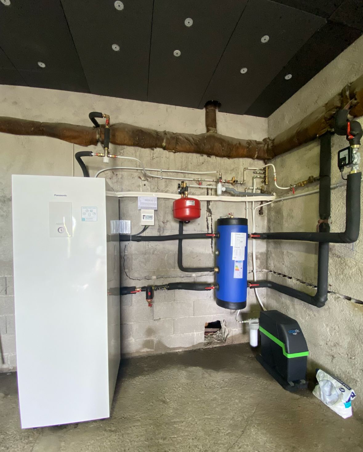 Chauffe-eau et système de chauffage blancs fixés au mur d'une buanderie. Tuyaux et commandes visibles.