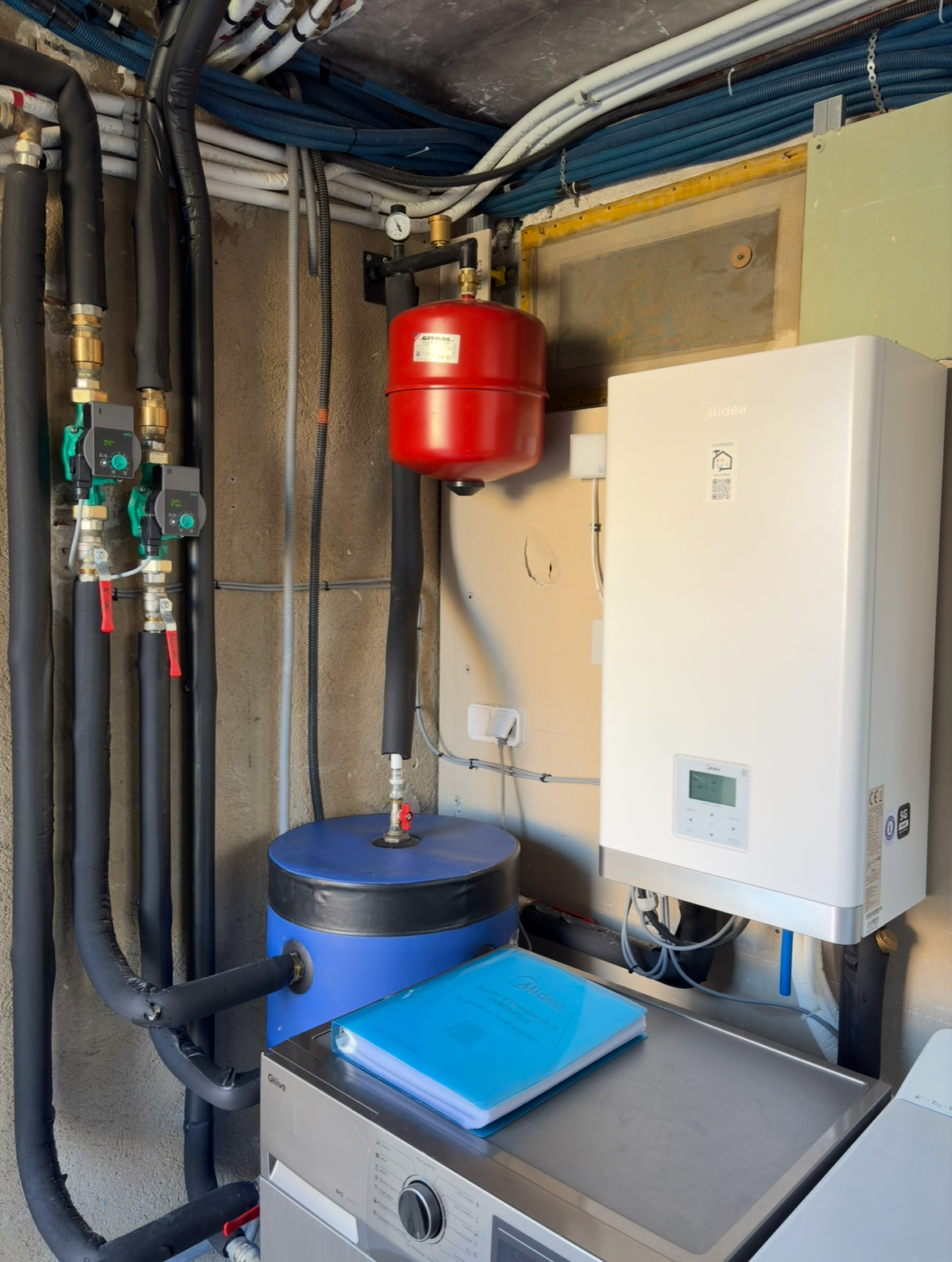 Unité de pompe à chaleur Panasonic extérieure, blanche avec logo bleu, à côté d'une clôture en bois.