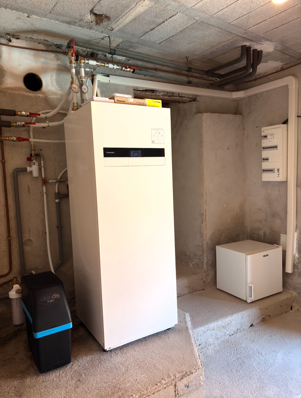 Chauffe-eau et système de chauffage blancs fixés au mur d'une buanderie. Tuyaux et commandes visibles.