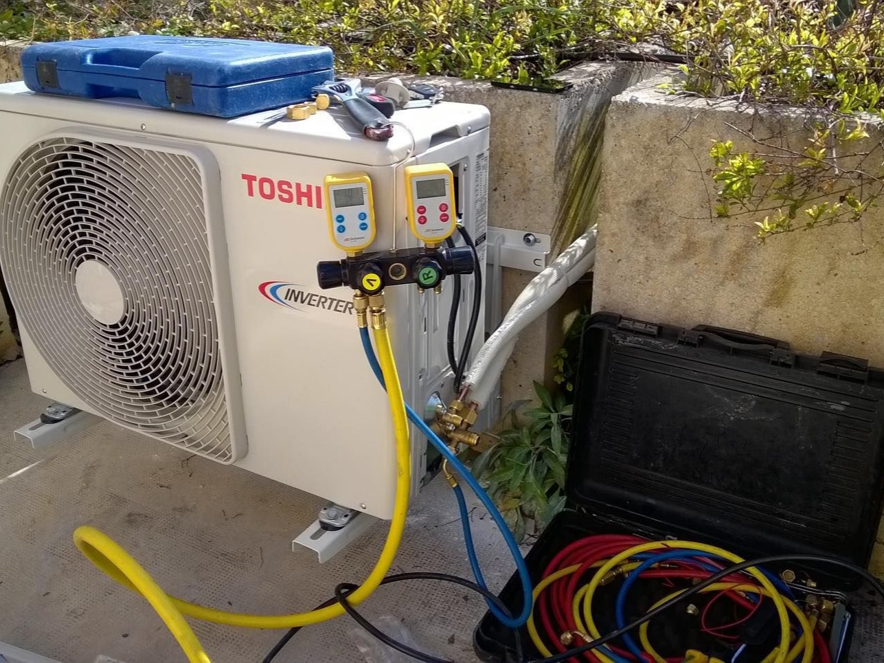 Unité de climatisation extérieure avec manomètres et tuyaux raccordés.