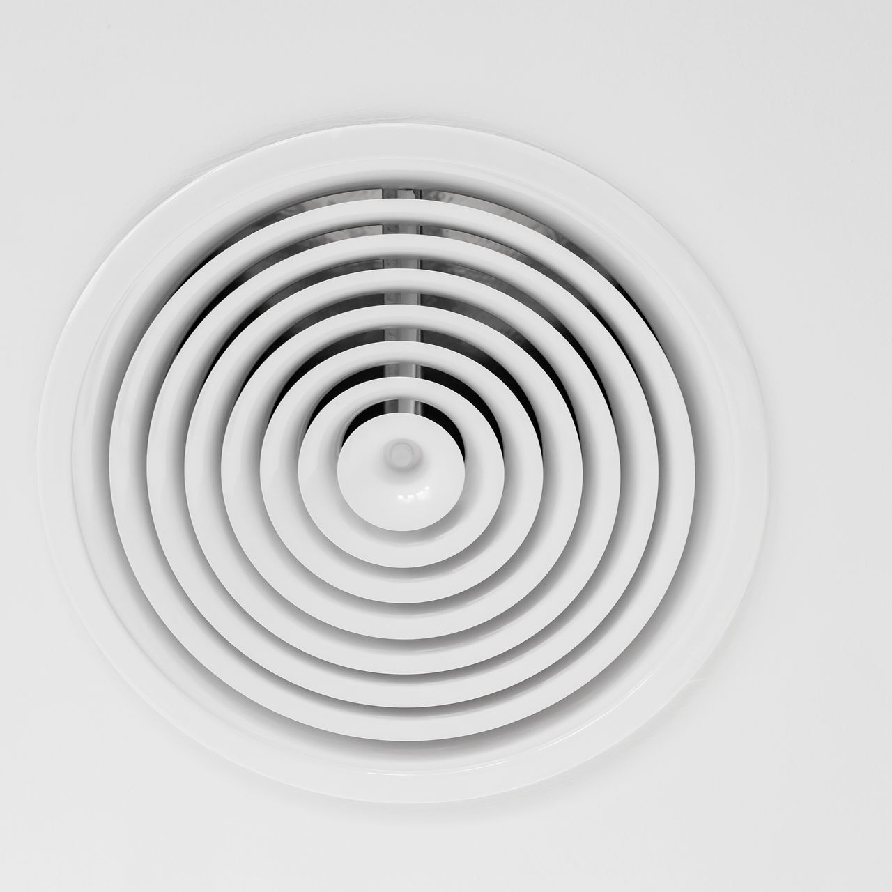 Grille d'aération circulaire blanche au plafond, avec anneaux concentriques et bouton central.