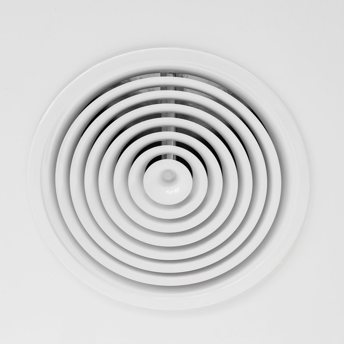 Grille d'aération circulaire blanche au plafond, comportant des anneaux concentriques.