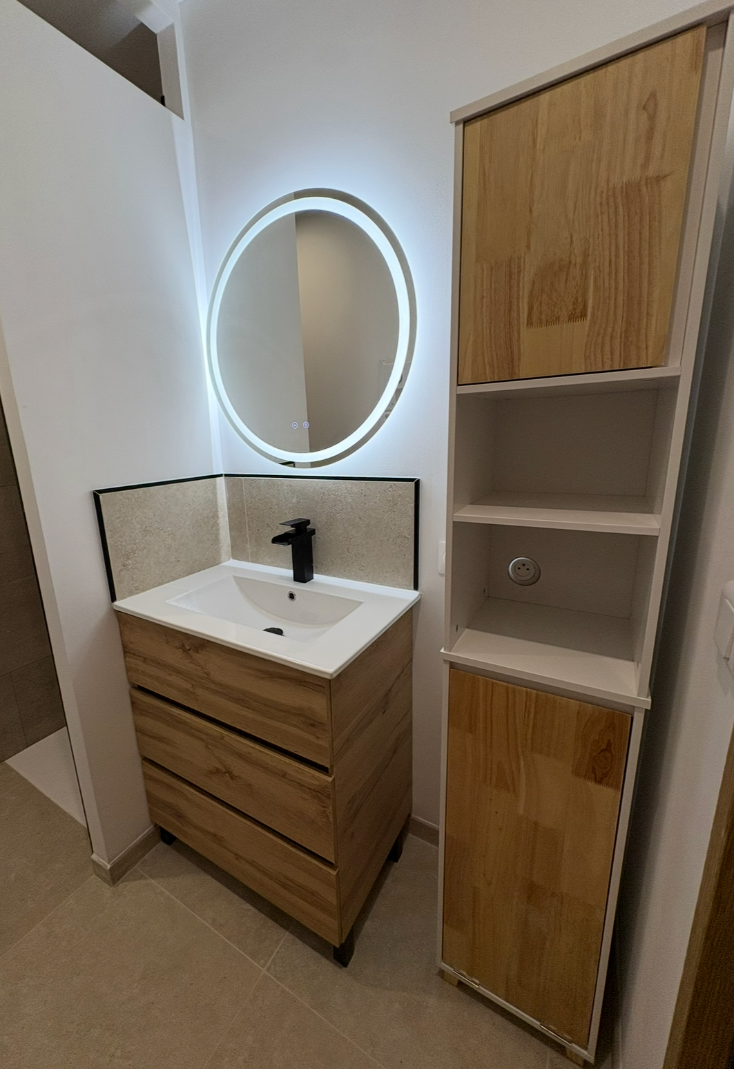 Salle de bains avec lavabo, miroir, toilettes, porte-serviettes et armoire en bois ; carrelage beige.