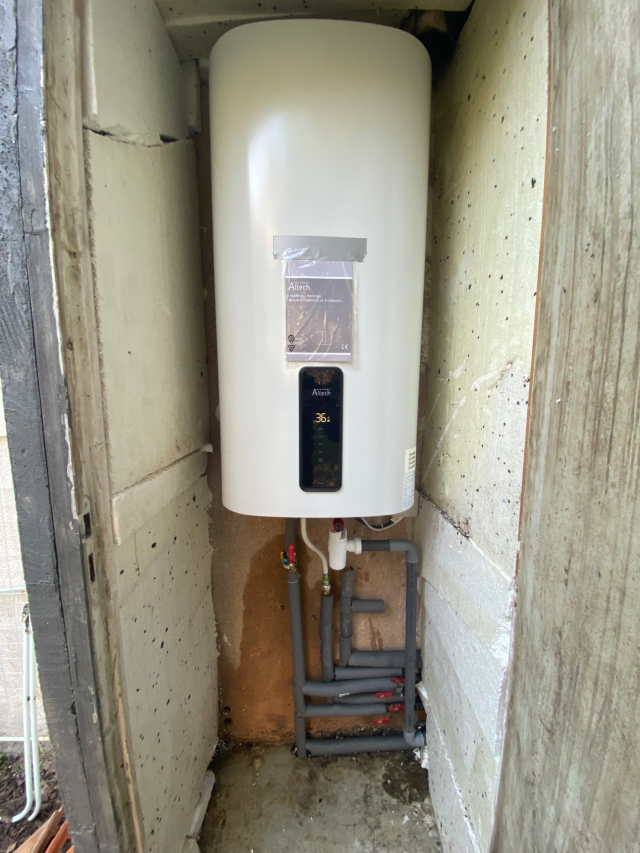 Chauffe-eau blanc de grande taille, fixé sur un mur carrelé dans une cuisine.