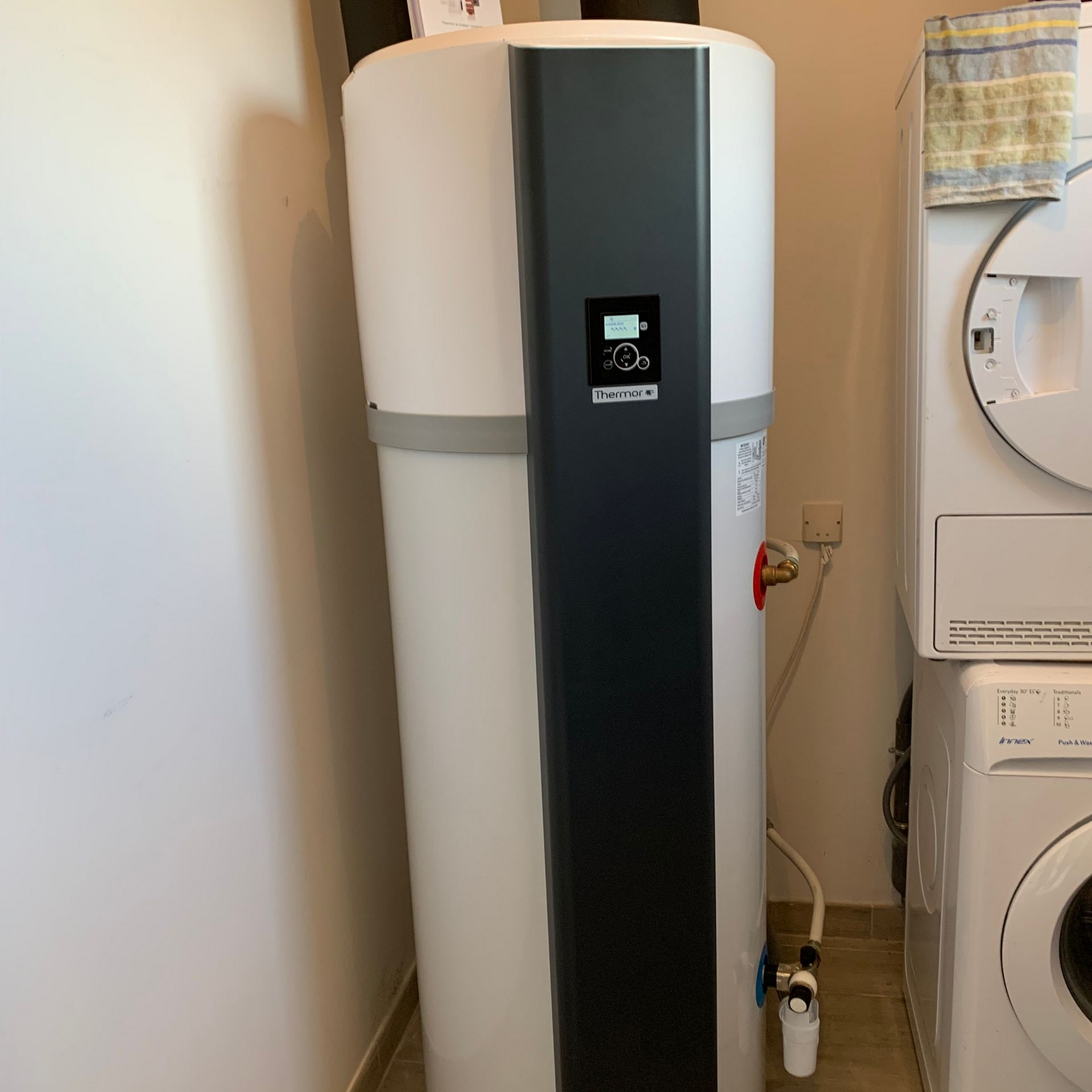 Chauffe-eau blanc et noir à côté d'une machine à laver et d'un sèche-linge dans une buanderie.