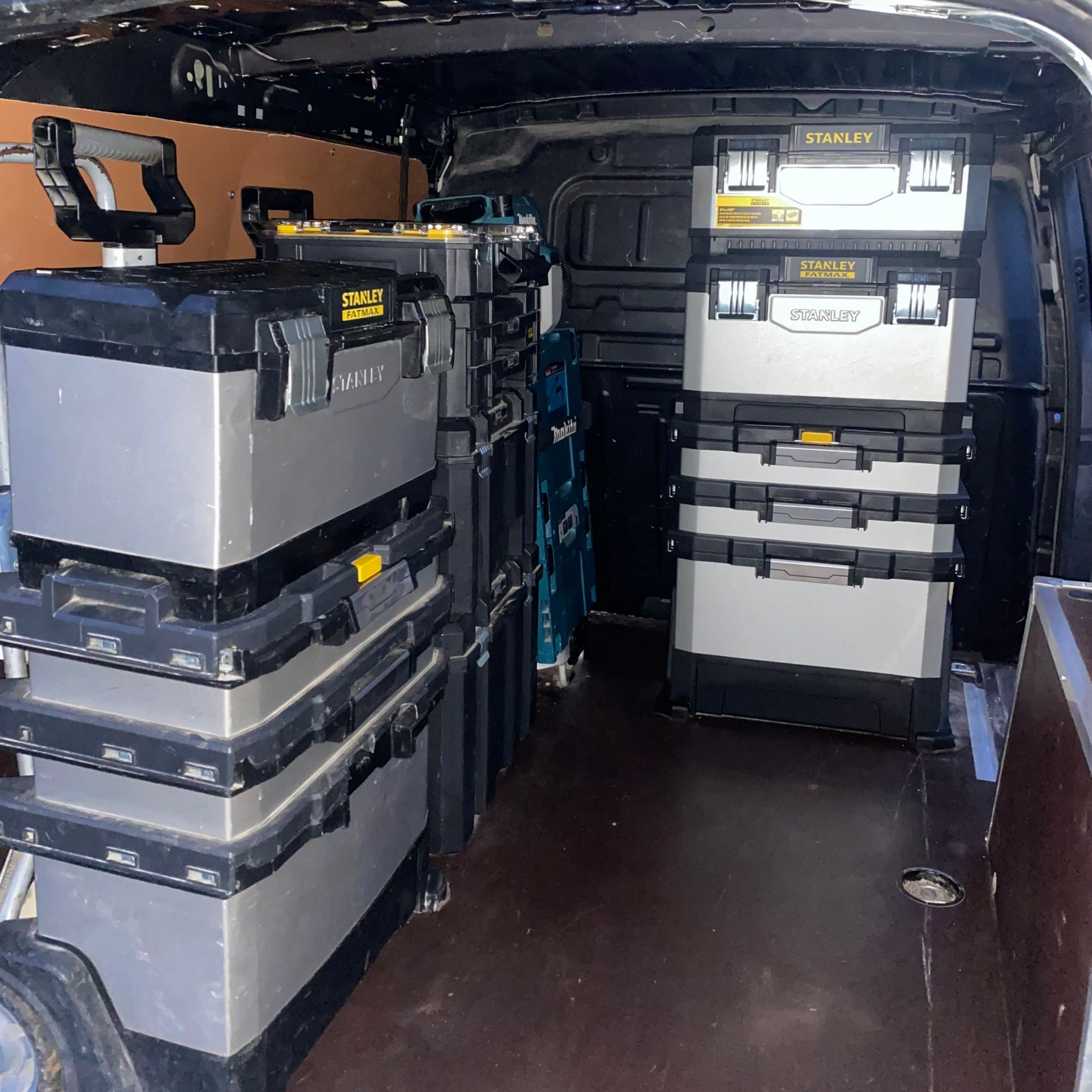 À l'intérieur d'une camionnette de travail, on aperçoit des boîtes à outils empilées.