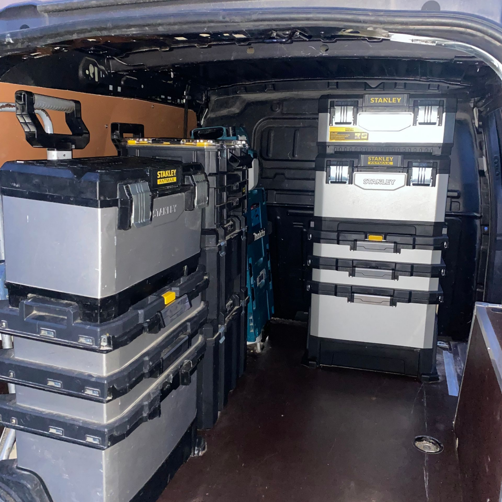 Intérieur d'une fourgonnette remplie de boîtes à outils noires et grises empilées.