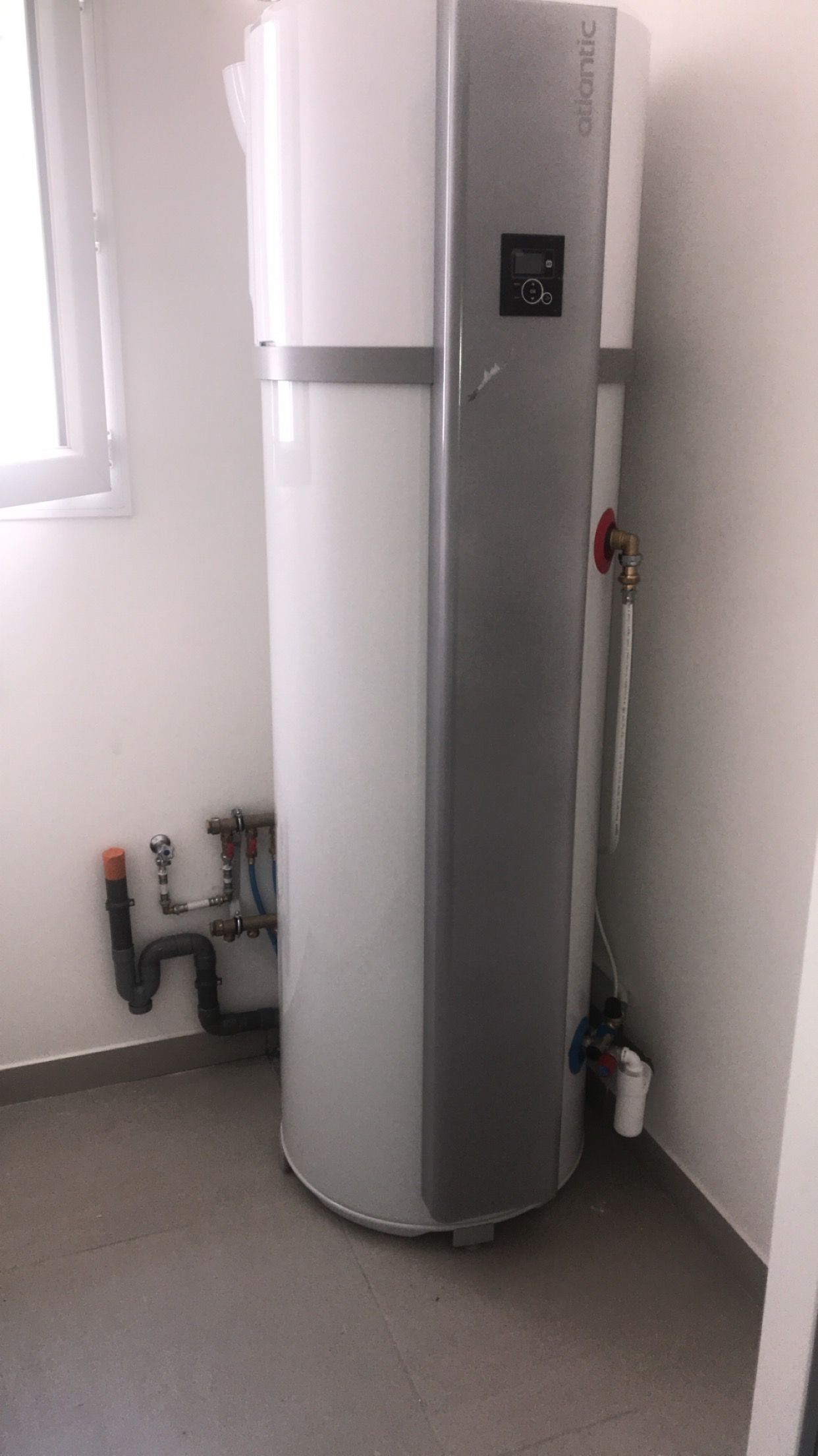 Composants bleus et blancs d'un système de chauffage fixés sur un mur blanc dans une buanderie.