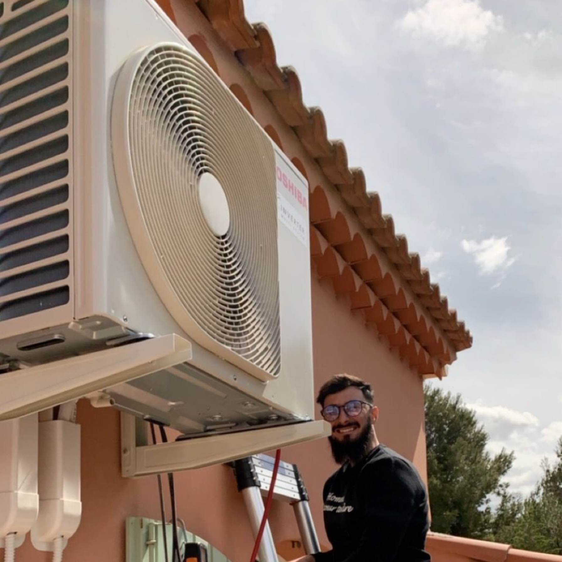 Loïc de LD-Energies à côté d'un climatiseur installé sur un bâtiment.