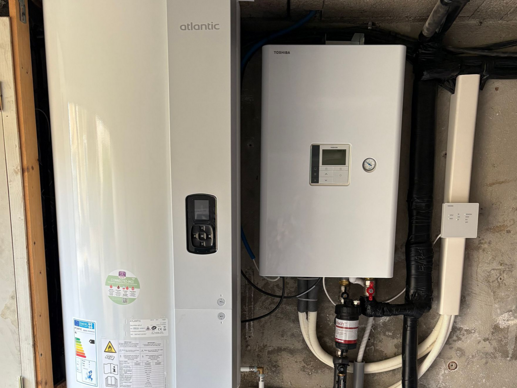 Chauffe-eau et élément chauffant blancs fixés sur un mur en béton. Tuyaux et câbles raccordés.