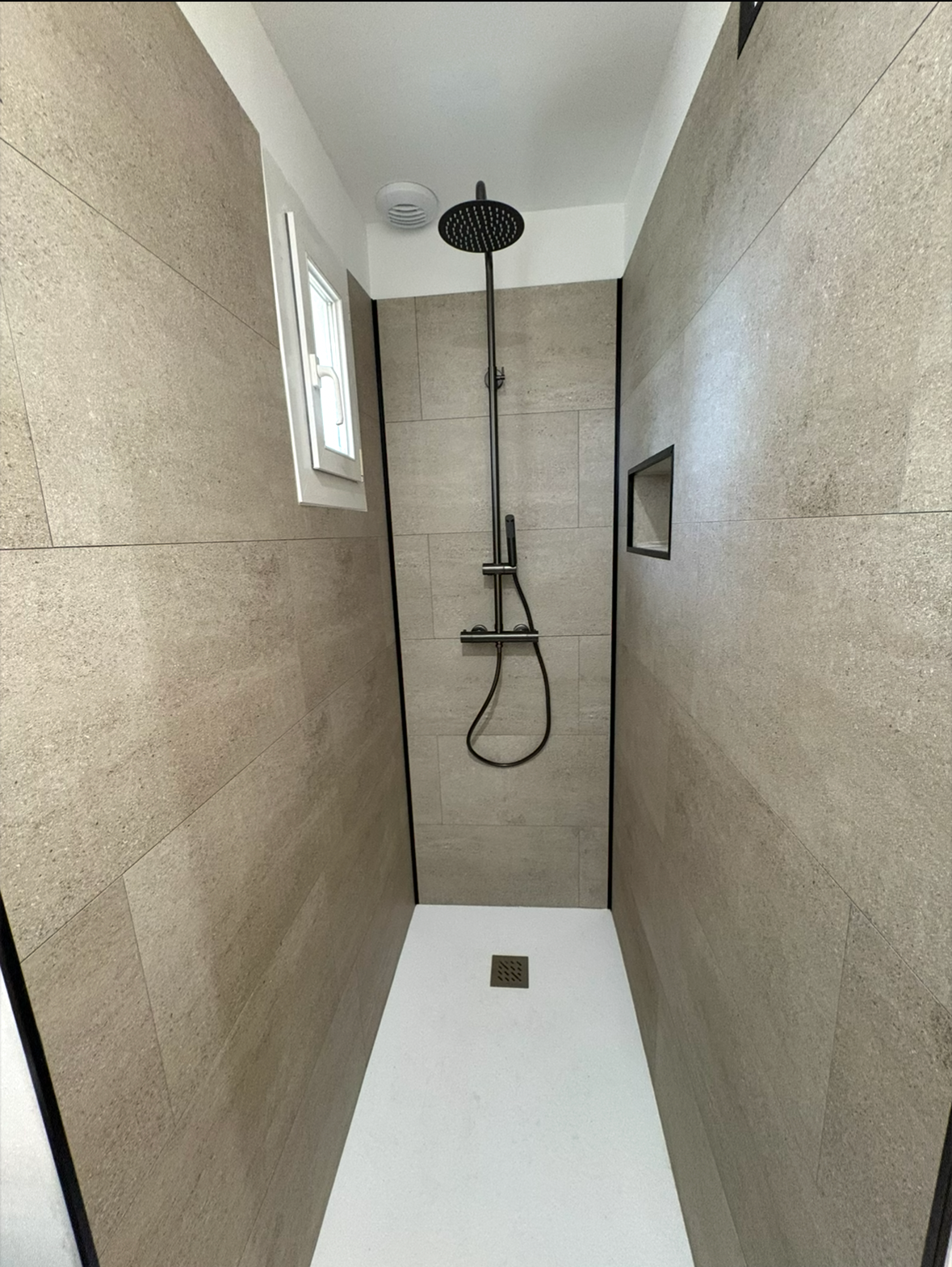 Baignoire blanche dans une salle de bains moderne aux murs et au sol carrelés de gris clair.