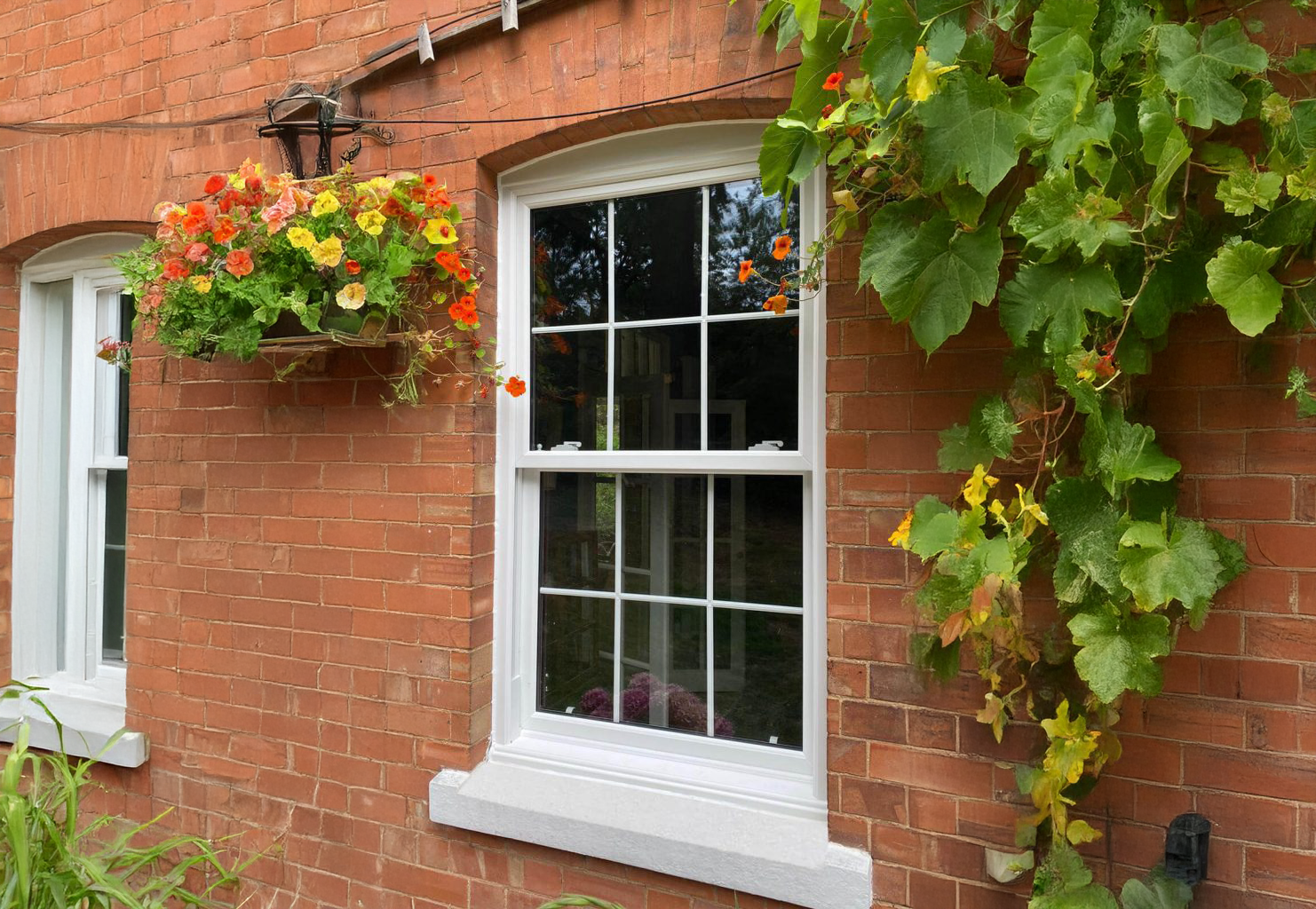 A brick building with a white window and a hanging basket of flowers.