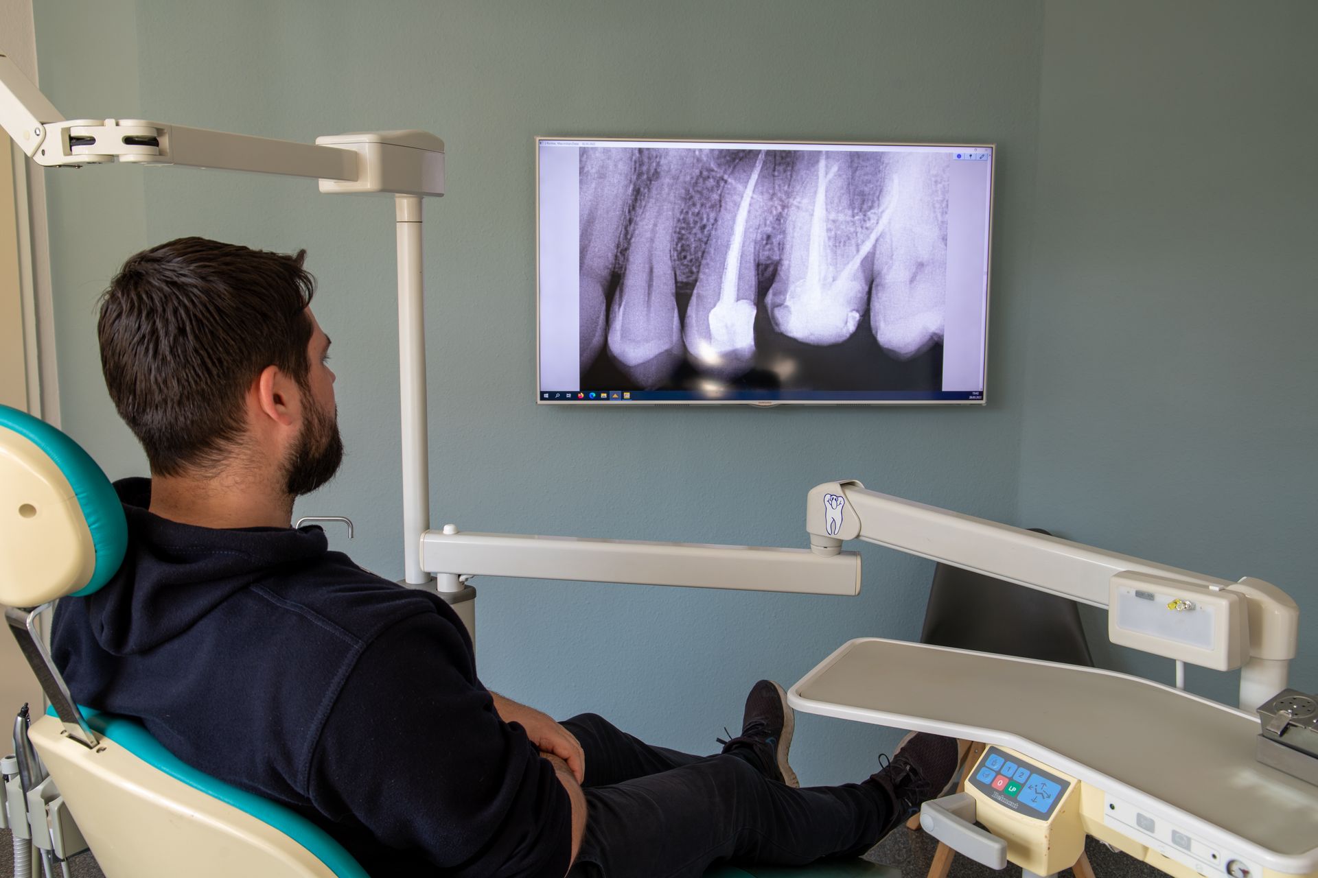 Ein Mann sitzt auf einem Zahnarztstuhl und betrachtet eine Röntgenaufnahme seiner Zähne, Zahnarztpraxis Enny Lohse.de