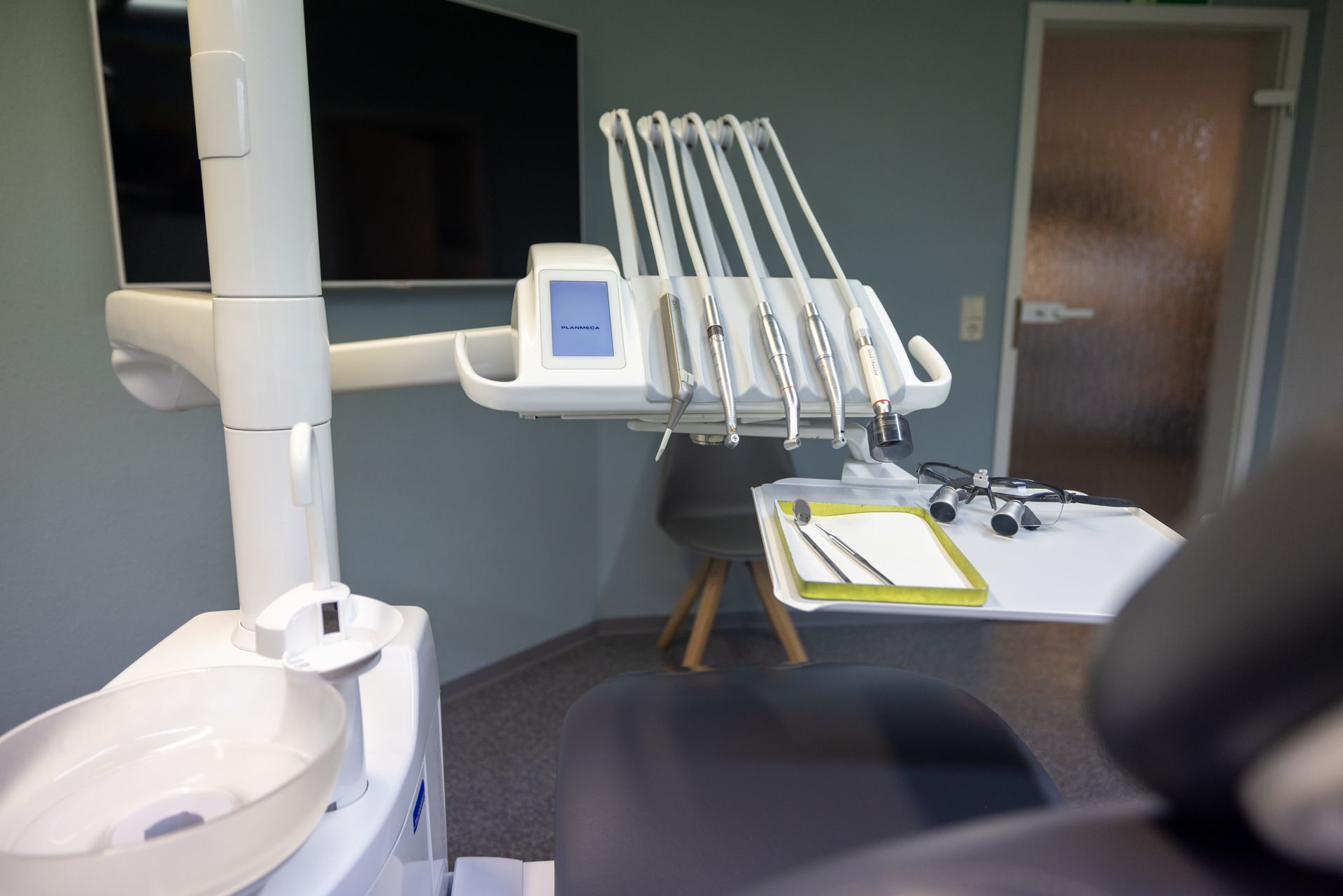 Ein Zahnarztstuhl in einer Zahnarztpraxis mit einem Monitor an der Wand, Zahnarztpraxis Enny Lohse.de