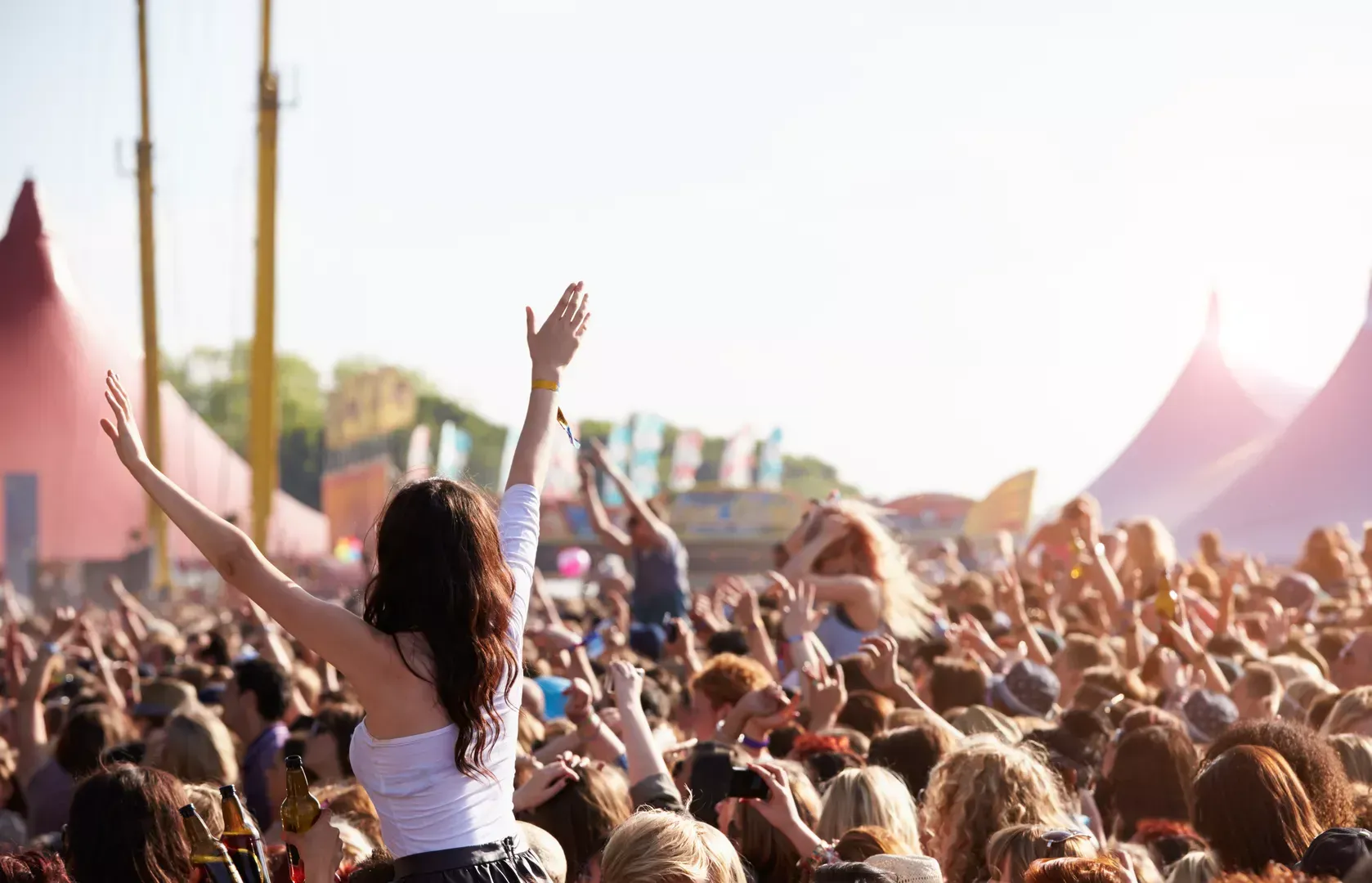 Menschenmenge bei einem Open-Air-Festival mit erhobenen Händen, im Hintergrund weiße Zeltspitzen.