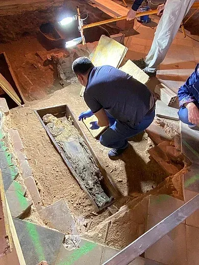 Un hombre está arrodillado frente a una momia en un ataúd.