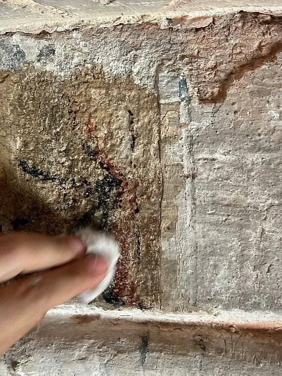 Una persona está limpiando una pared de ladrillos con un paño.