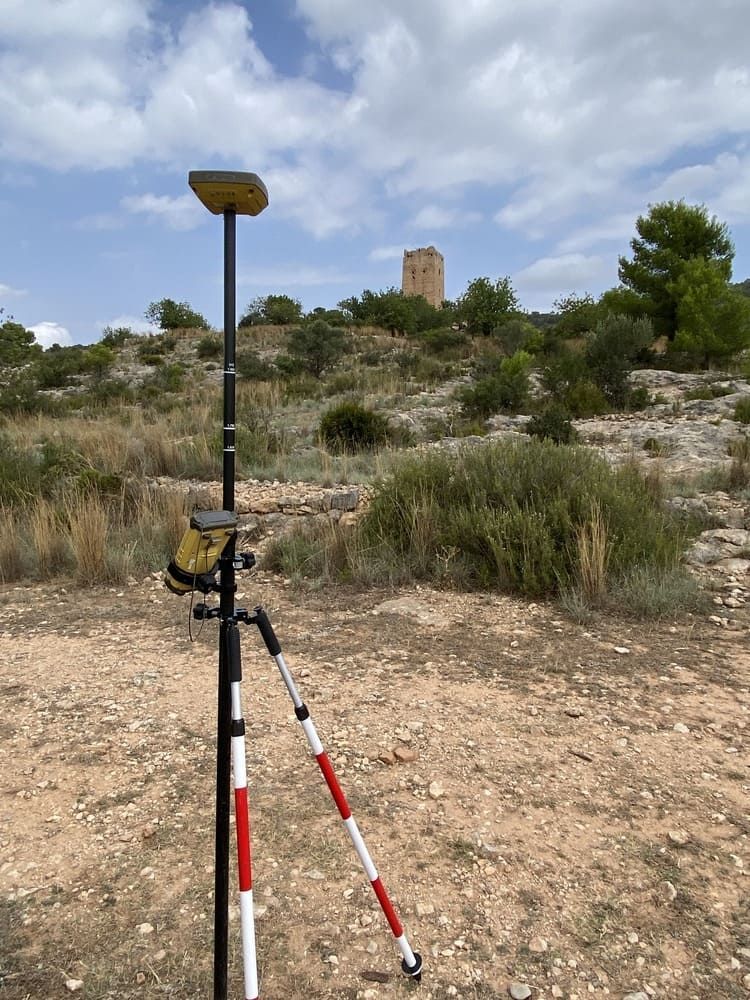 Un trípode está sentado en el medio de un campo de tierra con una torre al fondo.
