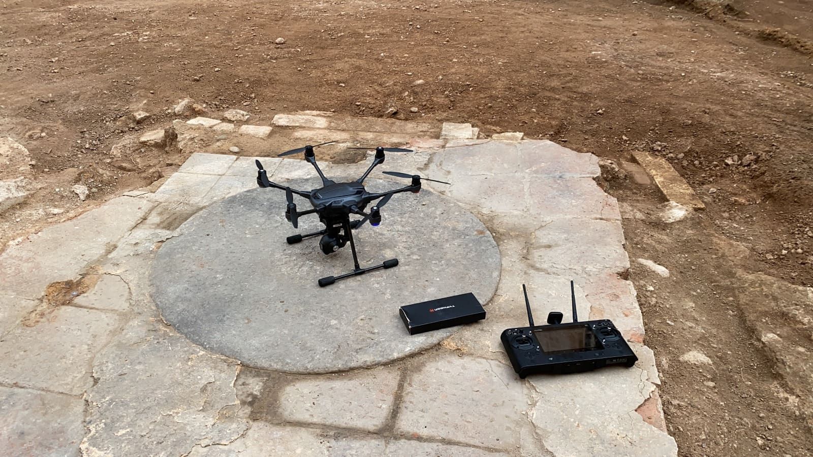 Un dron está sentado sobre una plataforma de piedra junto a un control remoto.