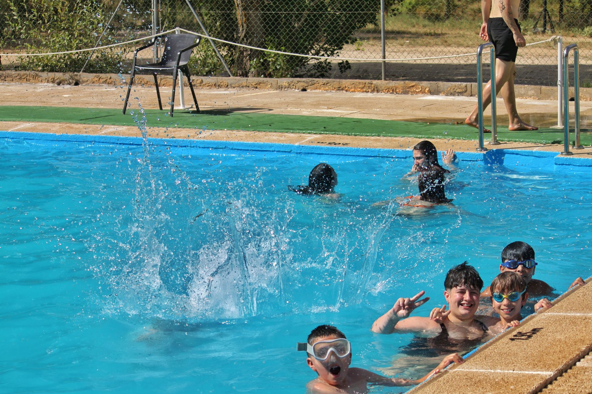 Gente nadando y chapoteando en una piscina al aire libre cerca del borde.