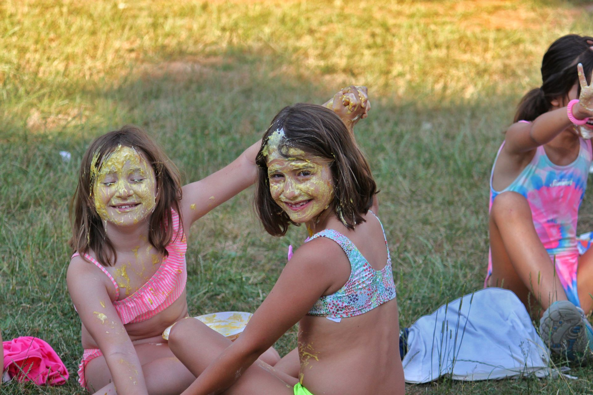 Dos niños con coloridos trajes de baño sentados en el césped al aire libre, sonriendo y charlando.