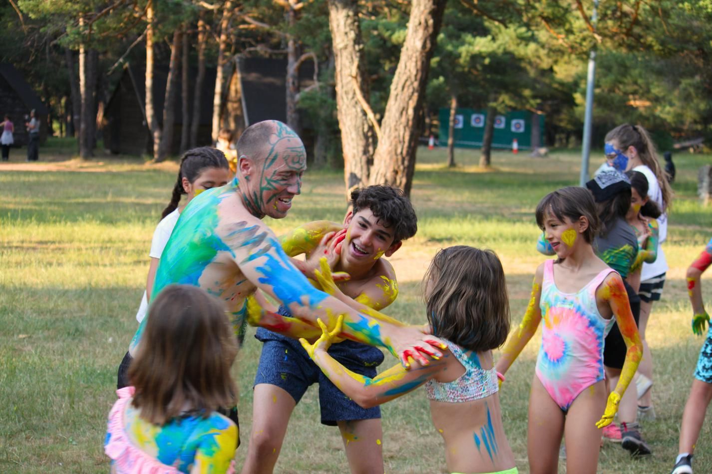Gente jugando con pintura de colores en un parque, sonriendo y cubiertos de salpicaduras brillantes.