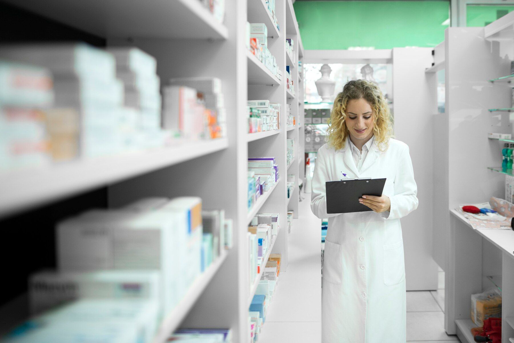 Donna in camice bianco in una farmacia, mentre controlla l'inventario dei farmaci sugli scaffali.