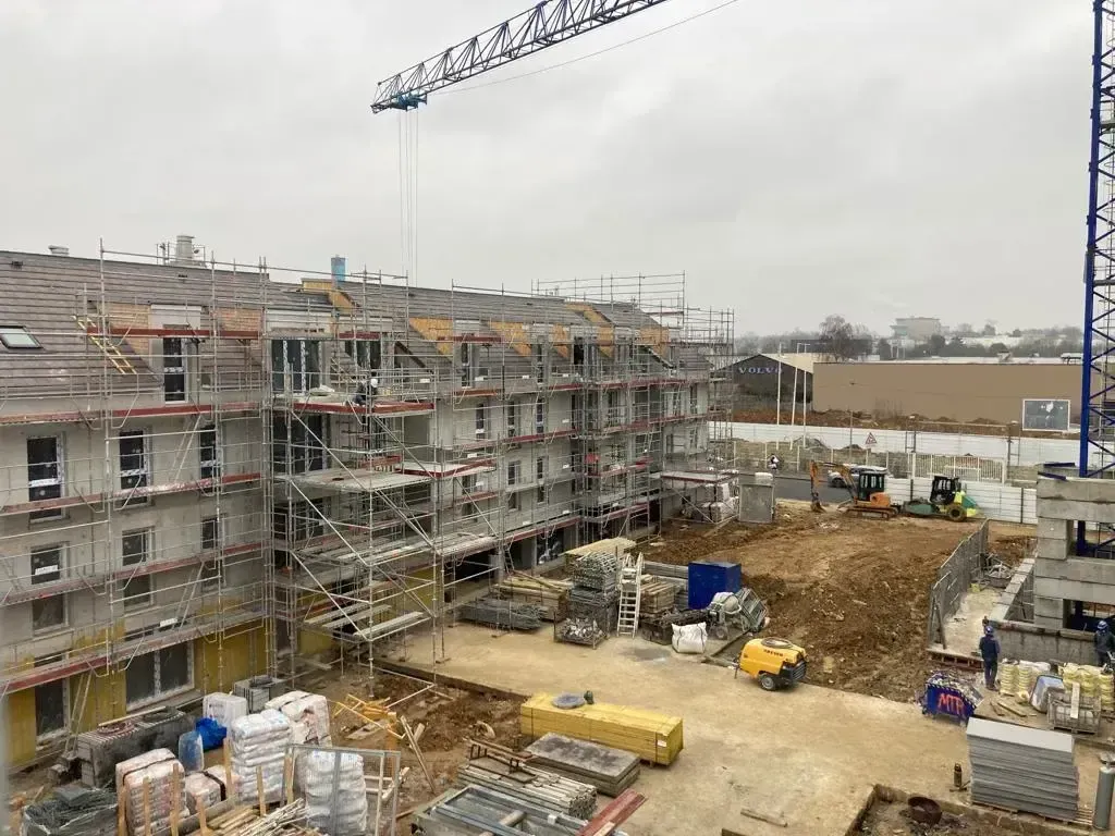 Immeubles résidentiels en construction, entourés d’échafaudages, avec une grue et un terrain en terre au premier plan