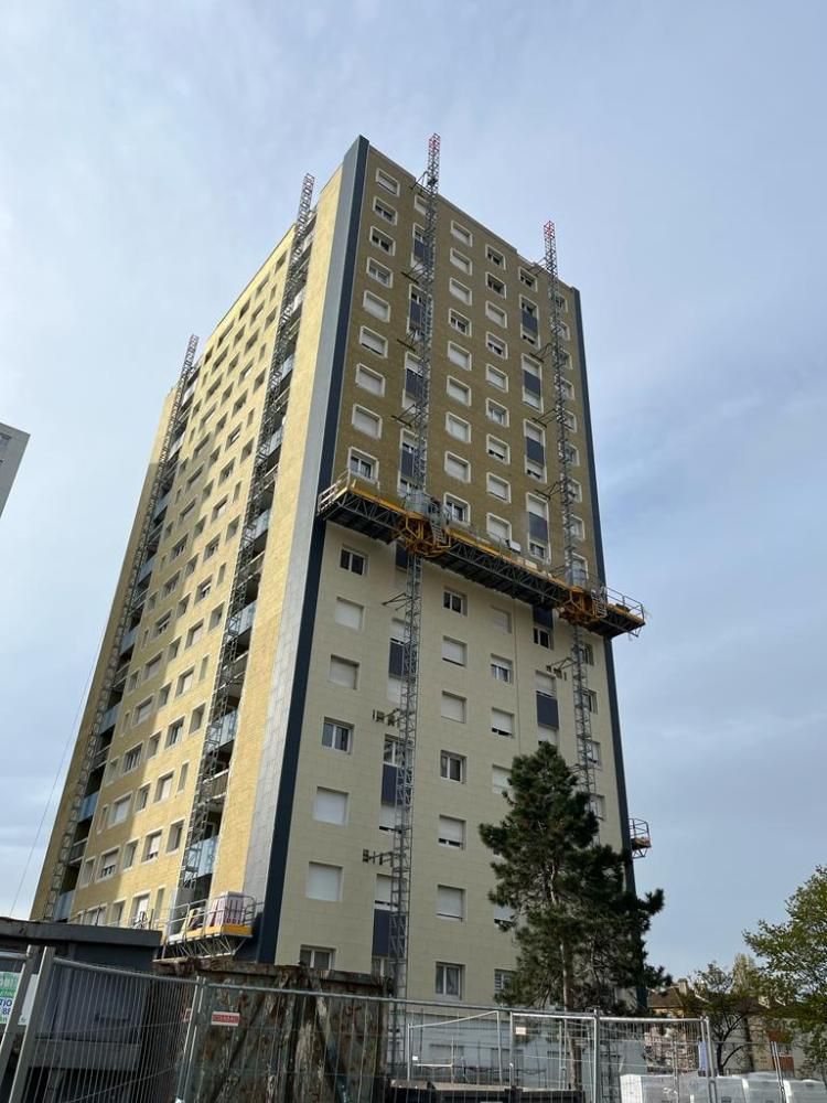 Immeuble beige de grande hauteur en construction, avec des échafaudages et un ciel bleu en arrière-plan