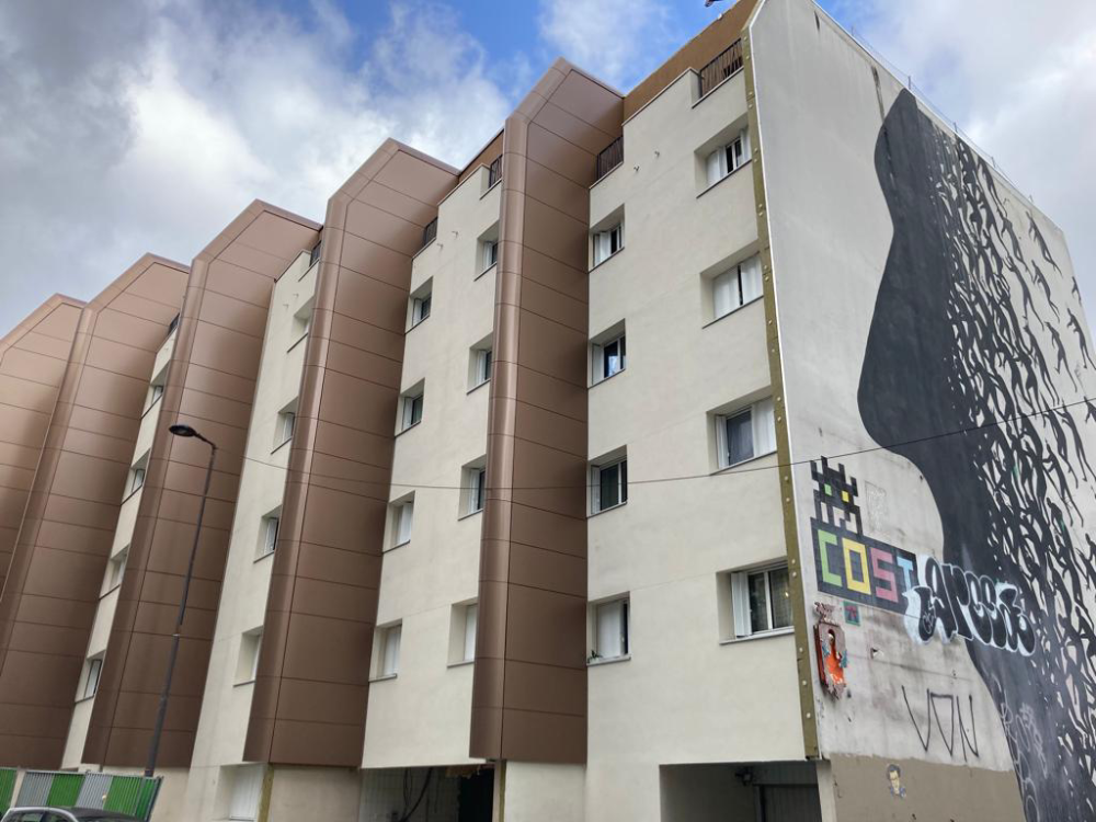 Extérieur d’un immeuble résidentiel aux façades brunes et blanches, avec une grande fresque murale sur le côté