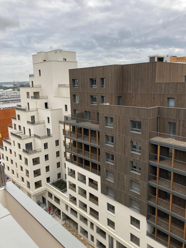 Immeubles résidentiels modernes aux façades blanches et brunes sous un ciel nuageux, vus d’en haut