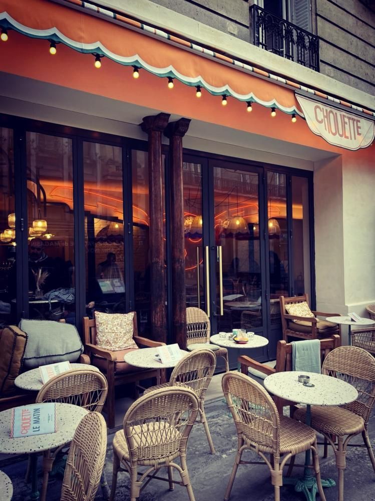 Terrasse de café en plein air avec des chaises et des tables en osier sous un auvent orange, au crépuscule