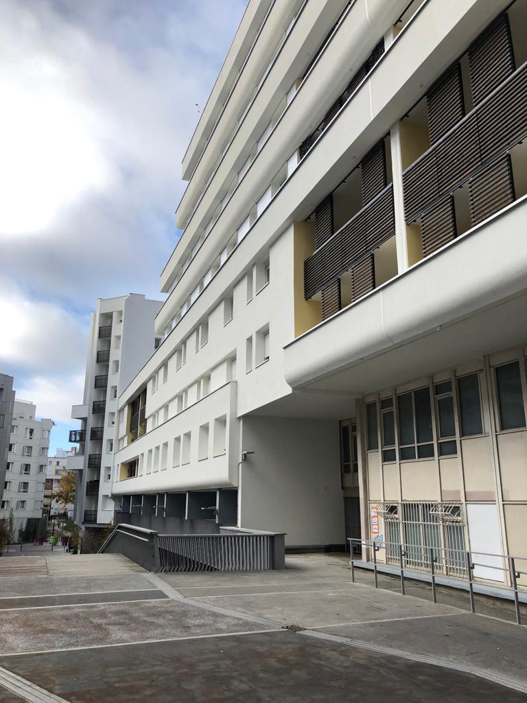 Immeuble moderne blanc avec des balcons donnant sur une cour pavée à ciel ouvert, sous un ciel nuageux