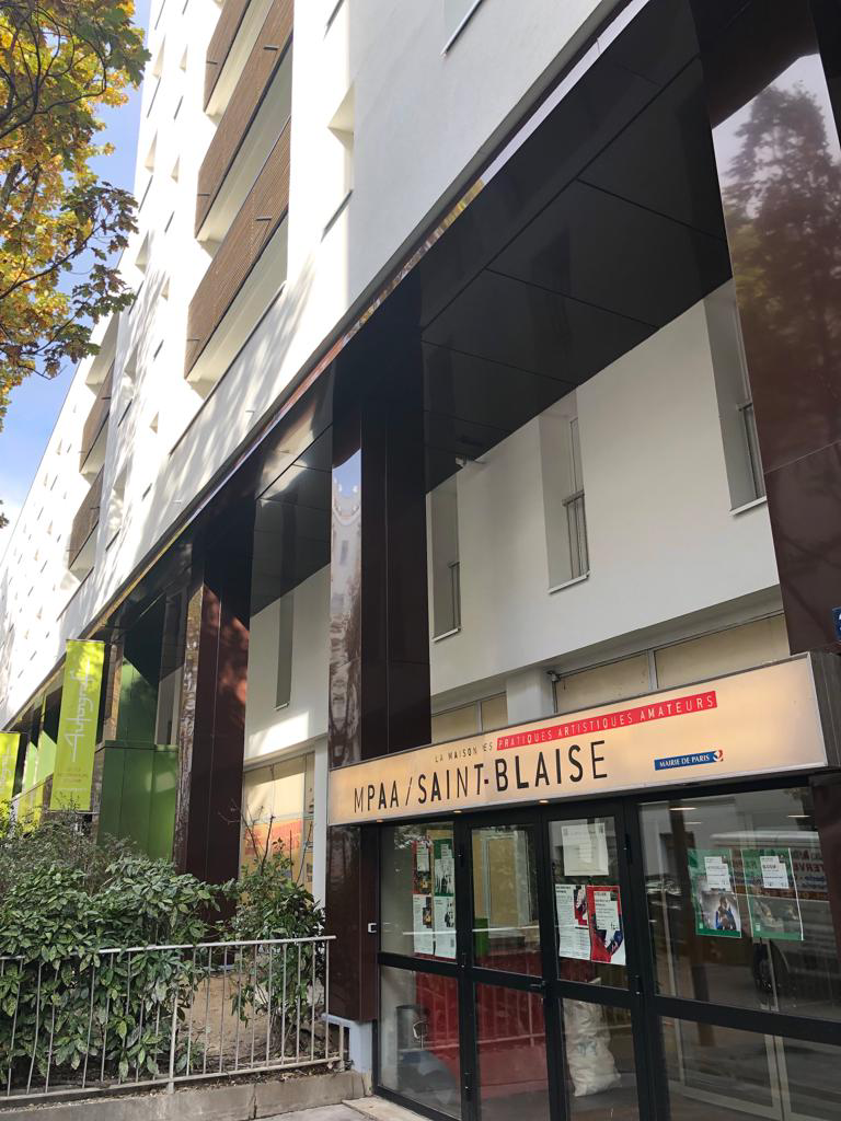 Local commercial moderne au rez-de-chaussée d’un immeuble résidentiel, avec des portes vitrées, un auvent noir et des barrières le long du trottoir