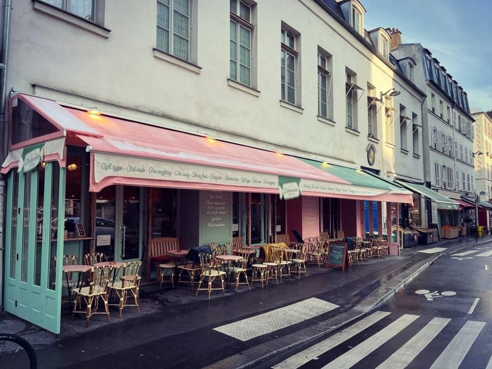Café de rue avec des stores roses et des tables en terrasse, le long d’une rue calme d’une ville au style européen
